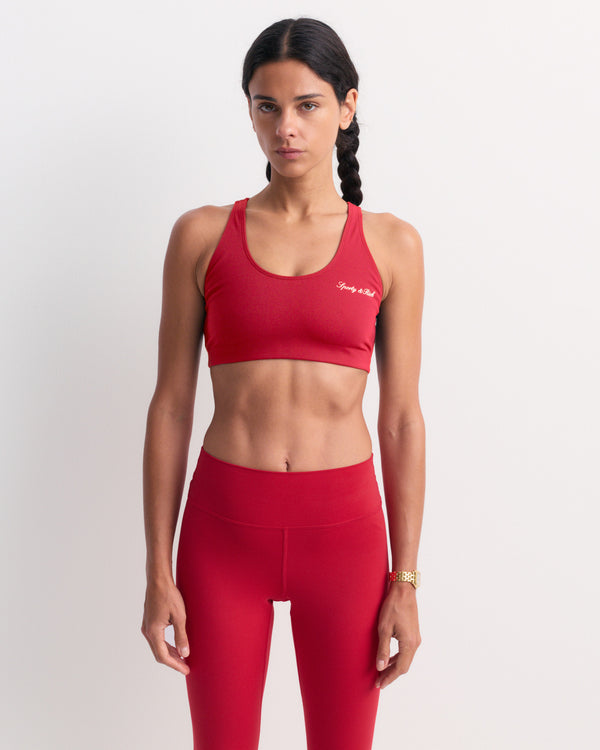A woman in the Billie Signature Logo Sports Bra - Ruby stands against a plain white background, looking forward.
