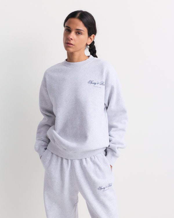 Emmett Club Script Crewneck in Heather Gray with small cursive text on the left chest, displayed on a white background. This relaxed fit sweatshirt channels the effortless appeal of vintage styles and is inspired by classic Sporty & Rich crewnecks.