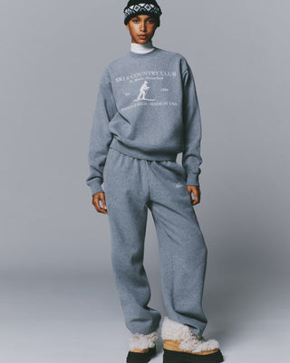 A person in an oversized LuxeFleece sweatshirt, Blakely Signature NY Wide Sweatpant, patterned beanie, and slippers.