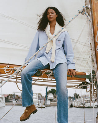 Woman sitting on a sailboat wearing a light blue jacket and jeans.