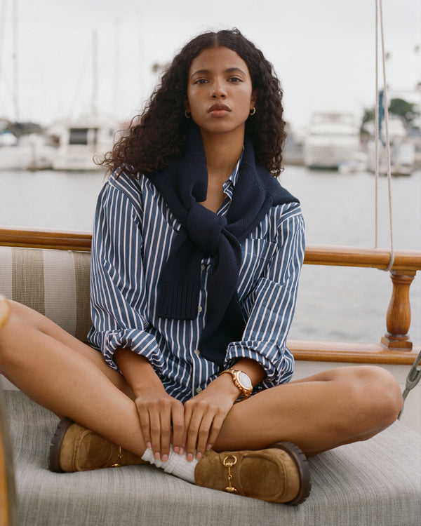 Woman sitting on a boat wearing a striped shirt, navy scarf, and brown boots.