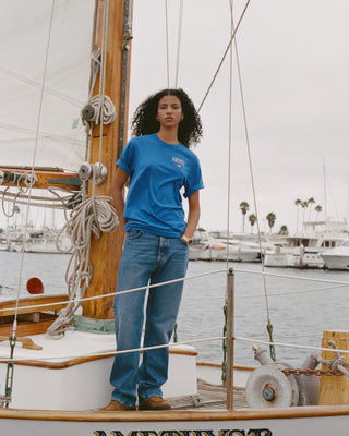 Person wearing a blue t-shirt and jeans standing on a boat with a marina in the background