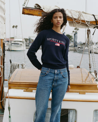 Woman wearing a navy blue sweater with 'Sporty & Rich' logo on a boat
