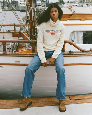 Woman sitting on a boat wearing a 'Sporty & Rich' sweater.