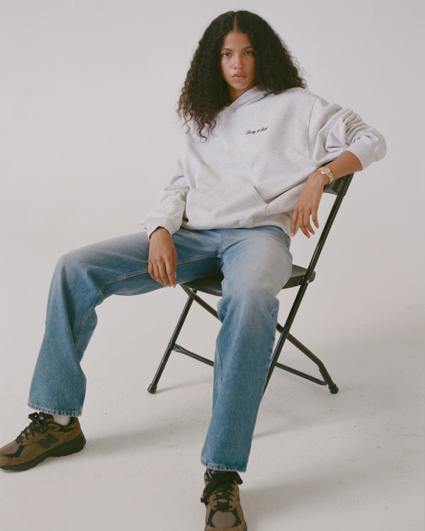 Person wearing a light gray sweatshirt and blue jeans sitting on a chair against a white background