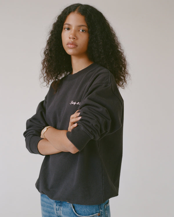 Person wearing a black sweatshirt with text, standing against a plain background