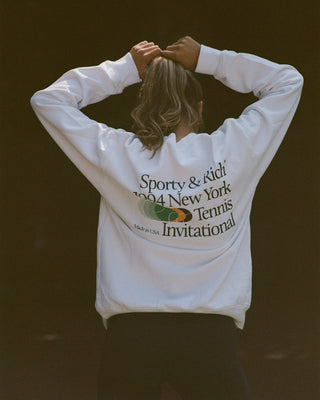 Person wearing a white sweatshirt with text and logo on the back, standing against a dark background