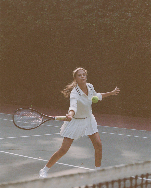 Woman playing tennis on a clay court with a racket and ball.