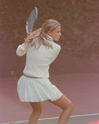Woman in a white tennis outfit holding a racket on a tennis court