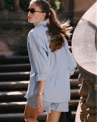 Woman in a light blue striped outfit walking outdoors.