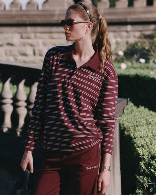 Woman wearing a maroon and black striped shirt with a logo, standing outdoors.
