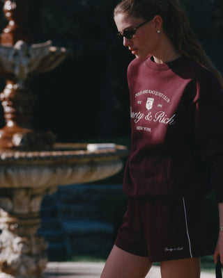 Woman wearing a burgundy sweatshirt with text and logo, standing in front of a fountain.