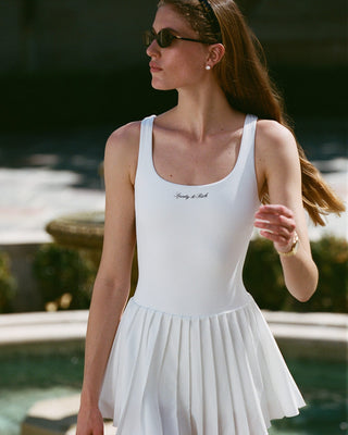 Woman wearing a white pleated dress with text, standing by a pool.