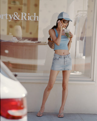 Woman in a blue top and denim skirt standing in front of a store window with 'Party & Rich' branding.
