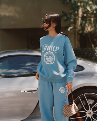 woman wearing a blue 'Juicy' sweatshirt and pants standing next to a car.