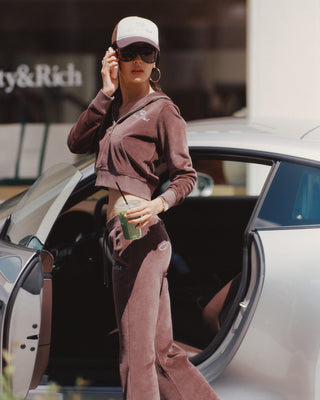 Person in a brown tracksuit stepping out of a car, holding a drink.