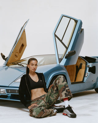 Woman sitting in front of a classic car with open doors on a white background