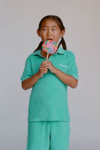 Young girl in a teal outfit holding a colorful lollipop against a plain background
