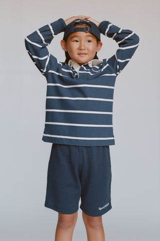 Child wearing a blue and white striped shirt and navy shorts on a plain background