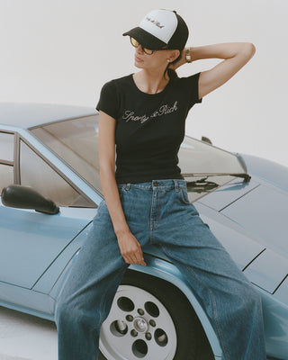 Person wearing a black t-shirt with text and blue jeans sitting on a light blue car.