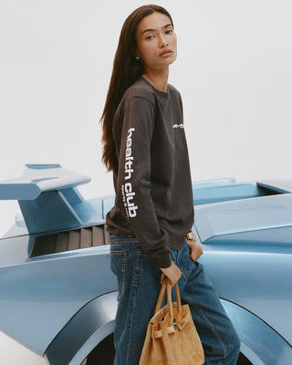 Person wearing a dark long-sleeve shirt with text, standing next to a futuristic vehicle.