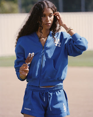 LA Serif Zip Hoodie in Team Blue/White, featuring a white LA logo on the left chest, front pockets, and a zip closure. Crafted from 100% cotton with an oversized fit and displayed laid flat on a white background.