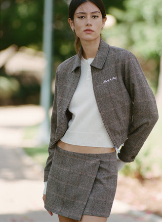 A woman models the Gyl Signature Logo Smart Zip Jacket in brown check with a matching skirt, standing with one hand on her hip against a plain background.