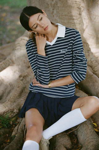 Person in a navy jacket, Abigail Signature Logo Abigail Skirt - Dark Navy, and cap stands against a plain white background.
