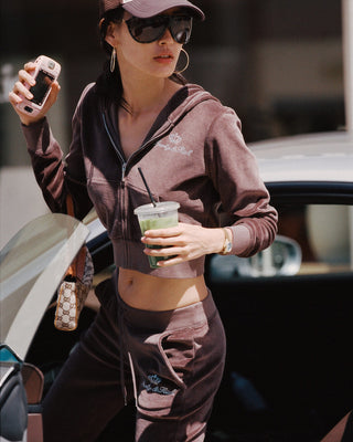 Woman in athletic wear holding a drink and phone, standing next to a car.