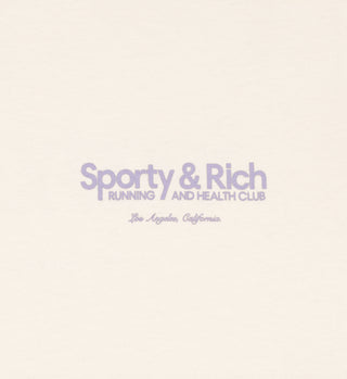 The Club T-Shirt - Cream/Faded Lilac features Sporty & Rich Running and Health Club, Los Angeles, California in purple on a light background. Made in the USA from 100% USA-grown cotton for comfort and style.