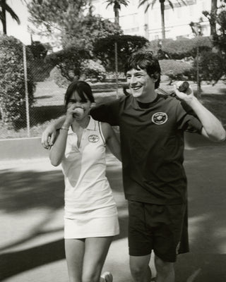 A young woman and man, dressed in tennis outfits featuring Eden Crest Gym Short - Navy/White, walk together smiling with arms around each other on a tennis court.