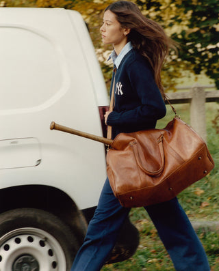 Woman walking with a brown leather bag and a white van in the background