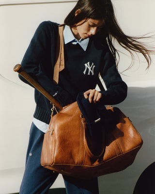Person holding a brown leather bag with a plain background