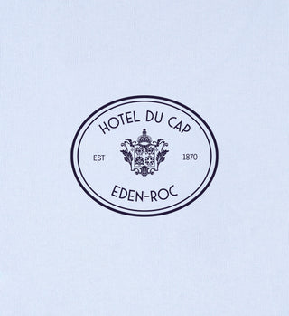 The Eden Crest T-Shirt - Ciel/Navy features the Hotel du Cap Eden-Roc crest logo, EST 1870, in an oval on a light background. Made from 100% cotton for ultimate comfort and style.