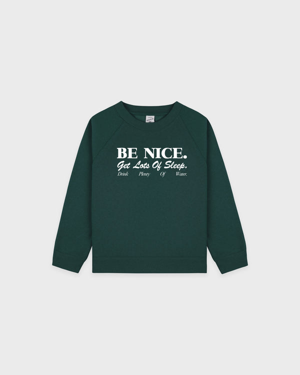 Introducing the Be Nice Kids Crewneck - Forest/White: this cozy kids sweatshirt features uplifting white text—BE NICE. Get Lots Of Sleep. Drink Plenty Of Water.—on a rich forest green background. Made from a soft cotton-polyester blend, its oversized fit ensures comfort and style for everyday wear.