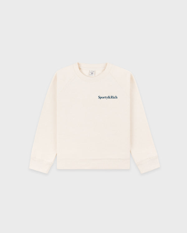 Eat More Veggies Kids Crewneck in Cream/Navy, featuring navy "Sporty & Rich" text on the left chest. Made from a soft cotton-polyester blend for comfort and durability, this oversized crewneck sweatshirt is available in kids sizes and is shown on a plain light background.