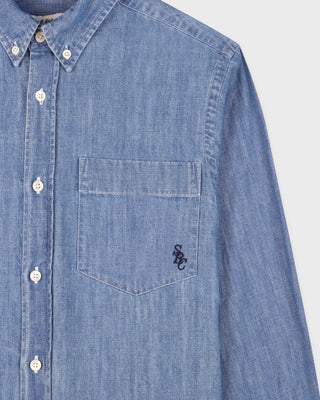 Blue denim shirt with a pocket and brand logo on a light gray background