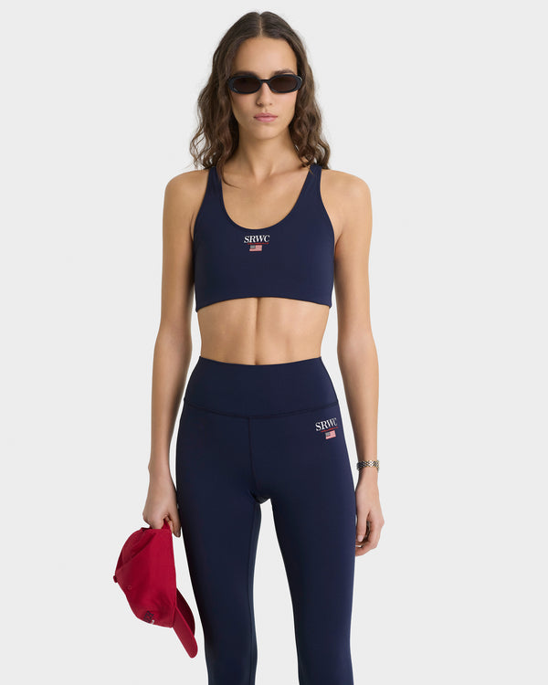 Woman wearing navy sports bra and leggings with a visible brand logo, holding a red jacket.