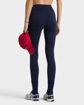 Person wearing navy leggings holding a red cap on a white background