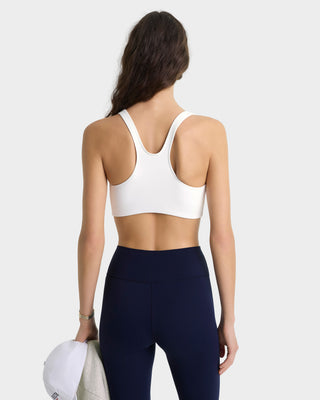 Woman wearing a white sports bra and navy leggings on a white background