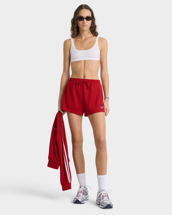 Woman wearing a white sports bra and red shorts, holding a red jacket on a white background
