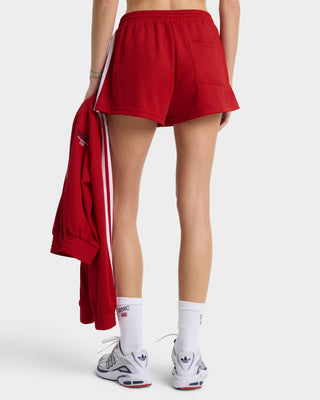 Person wearing red shorts with a white stripe, white socks, and Adidas shoes on a white background