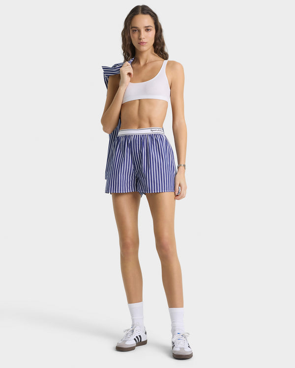 Woman wearing a white sports bra and blue striped shorts on a white background