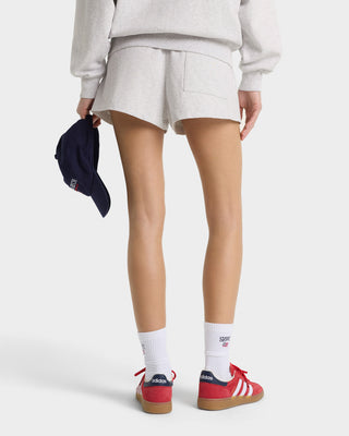 Person wearing white shorts, red Adidas sneakers, and white socks on a plain background
