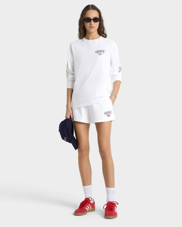 Woman wearing a white oversized sweatshirt and shorts set with red sneakers on a white background