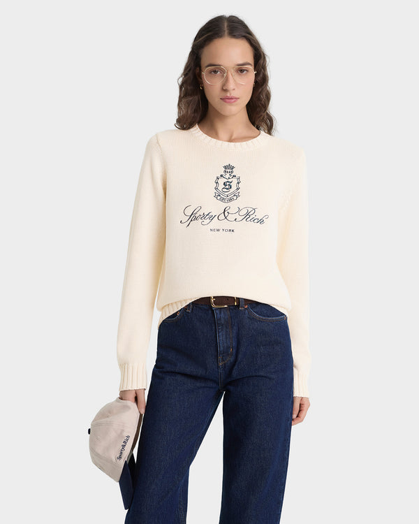 Introducing the Vendome Knitted Sweater in Ecru/Navy—a cream knit sweater with a cropped silhouette, detailed with “Spedy & Rich New York” and a black crest printed on the front. Crafted from 100% cotton for exceptional comfort, this piece is elevated by an embroidered logo for a refined finish.