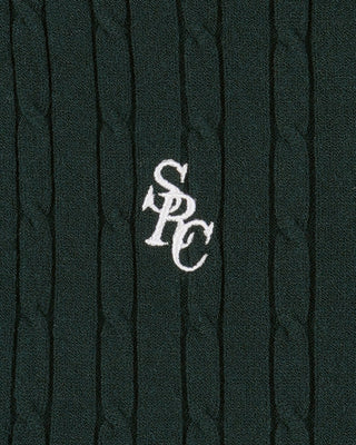 Dark green cable knit sweater with a white logo on a textured background