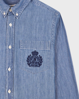 Blue denim shirt with a logo on the chest pocket against a light gray background