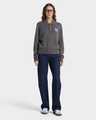 Person wearing a gray sweater with a logo and dark blue jeans on a white background