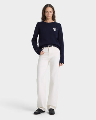 Person wearing a navy blue sweater with a logo and white pants on a white background
